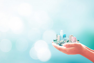 World environment day concept: Human hands holding city over blurred bokeh blue sky background