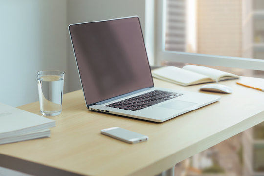 Close up desktop businessman, Wooden desk with modern laptop, glass of water, modern cell phone, notebook. Desktop with a view of downtown, Sunrise, Shallow DOF.