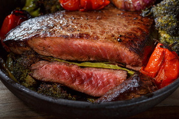 Beef steak medium rare with vegetables on a cast iron skillet. Still life of meat and vegetables in a low key. Rustic style food. covered with a rustic table