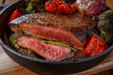 Beef steak medium rare with vegetables on a cast iron skillet. Still life of meat and vegetables in a low key. Rustic style food. covered with a rustic table