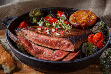 Beef steak medium rare with vegetables on a cast iron skillet. still life of food in low key. a dish of European cuisine. food in rustic style