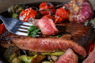 Beef steak medium rare pieces with a garnish of vegetables in a cast iron skillet. meat shot in low key. fatty foods rich in protein. ready meat dish in rustic style