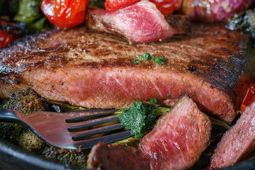 Beef steak medium rare pieces with a garnish of vegetables in a cast iron skillet. meat shot in low key. fatty foods rich in protein. ready meat dish in rustic style