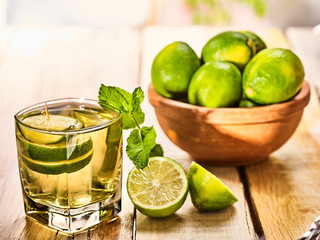 Country drink. On wooden boards is glass with green transparent drink and lime glue bowl. A drink number fifteen mojito with mint leaf on sunlight . Country life. Light background.