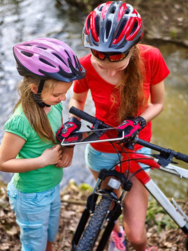 Bikes cycling girls. Girls children with tablet PC rides bicycle and searching way into internet map. Girl cycling fording throught water . Bicyclist is looking throught river.