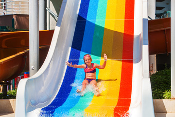 Child little girl on water slide at aquapark show hands up. There are some water slides with...
