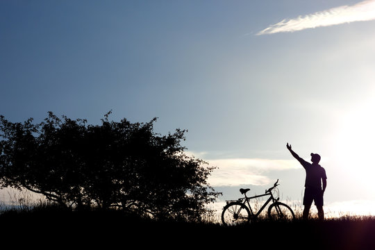 Silhouette of a man raising hand and bicycle on blue sky