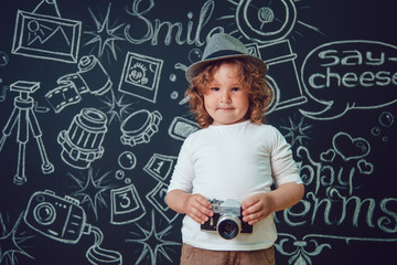 Little boy with a camera standing against a background of black walls with words