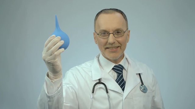 Happy smiled proctology doctor showing rubber syringe and looking at camera