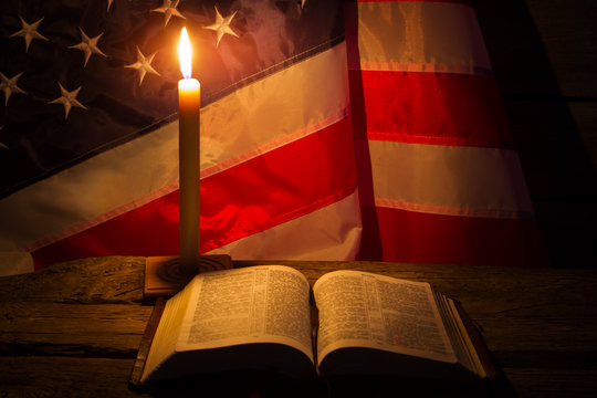 Burning candle and open book. America's flag behind burning candle. Night at old church. Never lose faith.