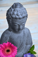 Close up of bronze brown stone Buddha statue with flowers in lotus position on  bamboo reed