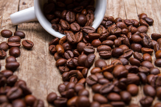 Cup with roasted coffee beans. Coffee grains of dark color. Fresh aroma of arabica. Cup on old brown shelf.