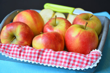 close up of red, yellow ,green apples in a wooden tray bowl with red white nostalgic  countryside checkered doily
