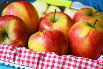 close up of red, yellow ,green apples in a wooden tray bowl with red white nostalgic  countryside checkered doily
