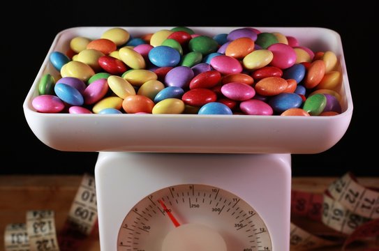 Many small colorful candy dish on kitchen scales, tape measure in the background
