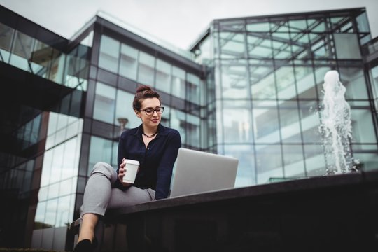 Woman using laptop while sitting against office building