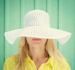 Beautiful blonde girl hiding behind hats fields