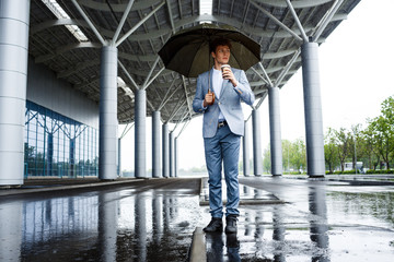 Handsome redhaired businessman with umbrella drinking coffee in the street