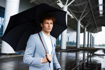 Portrait of  young redhaired businessman holding black umbrella in rainy street © Cookie Studio