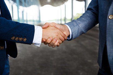 Picture of two young businessmen on street background shaking hands
