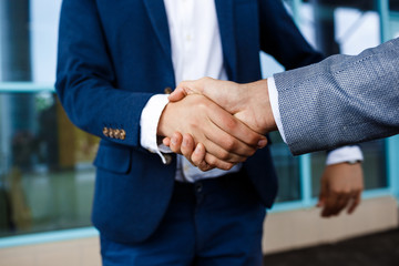 Picture of two young businessmen on street background shaking hands