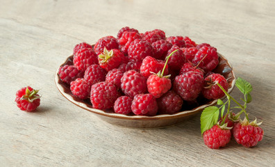 Ripe sweet raspberries in bowl on wooden table