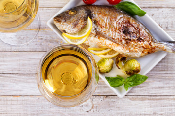 Glasses and bottle of white wine. Grilled dorado fish with vegetables in white plate. View from above, top studio shot