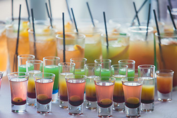 Beautiful row line of different colored alcohol cocktails on a party, martini, vodka,and others on decorated catering bouquet table on open air event, picture with beautiful bokeh
