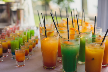 Beautiful line of different colored cocktails with smoke on a party, tequila, martini, vodka, and others on decorated catering bouquet table on open air party