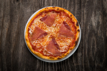 Round pizza with prosciutto on wooden background