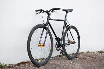 Fototapeta na wymiar Black fixed-gear bicycle standing near gray wall