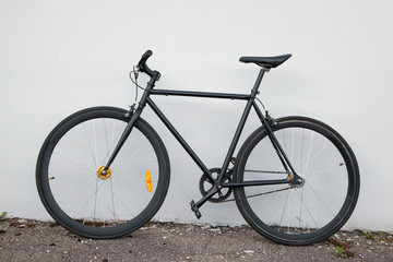 Black fixed-gear bicycle  standing near gray wall