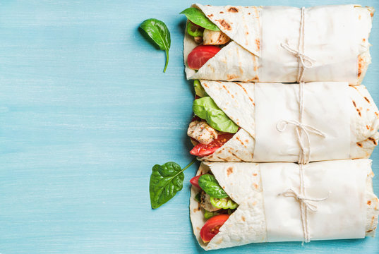 Healthy lunch snack. Three tortilla wraps with grilled chicken fillet and fresh vegetables over turquoise blue painted wooden background. Top view, copy space