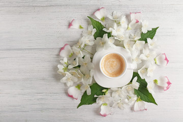 Cup of coffee with fresh flowers lying around on wooden background