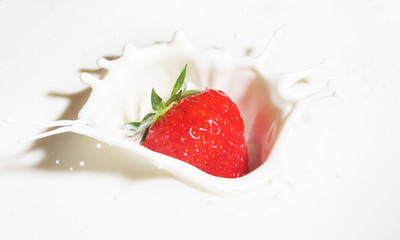 Strawberries falling into milk with splashes