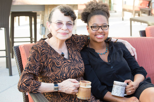 Closeup portrait, granddaughter and grandmother sitting, enjoying drinks coffee and tea together, isolated outdoors background