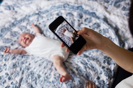 Mother taking picture of her baby from mobile phone in bedroom