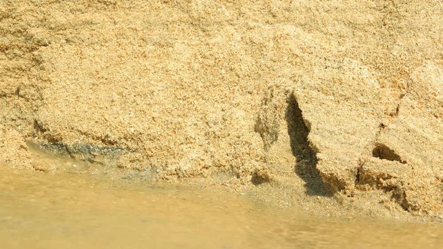 Flowing water continues to undercut and erode the loose, sandy walls of a washed out drainage canal, damaged by previous flooding. Video UltraHD