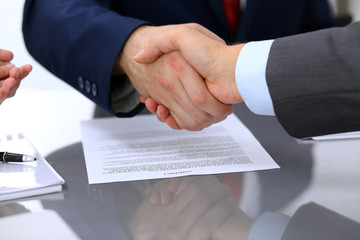 Two business man shaking hands to each other above signed contract