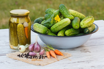 Cucumbers in metal bowl, spices for pickling and jar pickled cucumbers on table