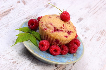 Fresh baked cupcake and raspberries on plate on old wooden background, delicious dessert