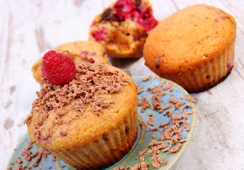 Baked muffins with raspberries and grated chocolate on wooden background, delicious dessert