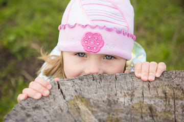 Pretty little girl peeks out from behind the stump
