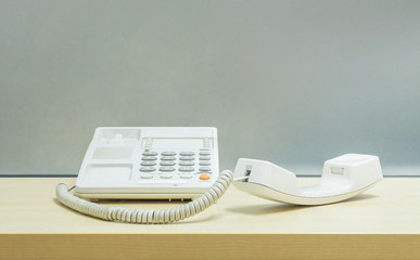 Closeup white phone , office phone on blurred wooden desk and frosted glass wall textured background in the work office