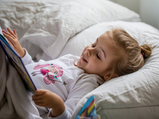 Obraz na płótnie Canvas little girl reads a children's book in bed after sleep