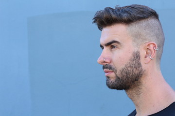 Profile view of handsome stylish young man with undercut hairstyle, beard and piercings with copy space