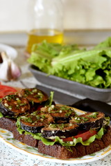 Sandwiches with fried eggplant, fresh tomato, lettuce, dill and garlic in a dish. Lettuce, olive oil, garlic, knife on the kitchen table. Cooking in kitchen