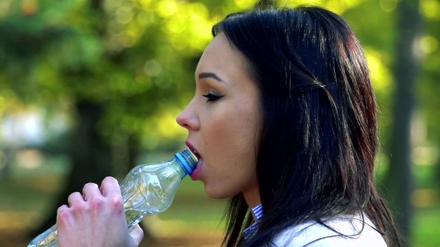 Slowmotion young beautiful woman stands and drinks from plastic bottle