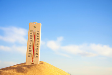 Thermometer with celsius scale on warm beach sand showing extreme high temperature.