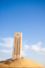Thermometer with celsius scale on warm beach sand showing high temperature.